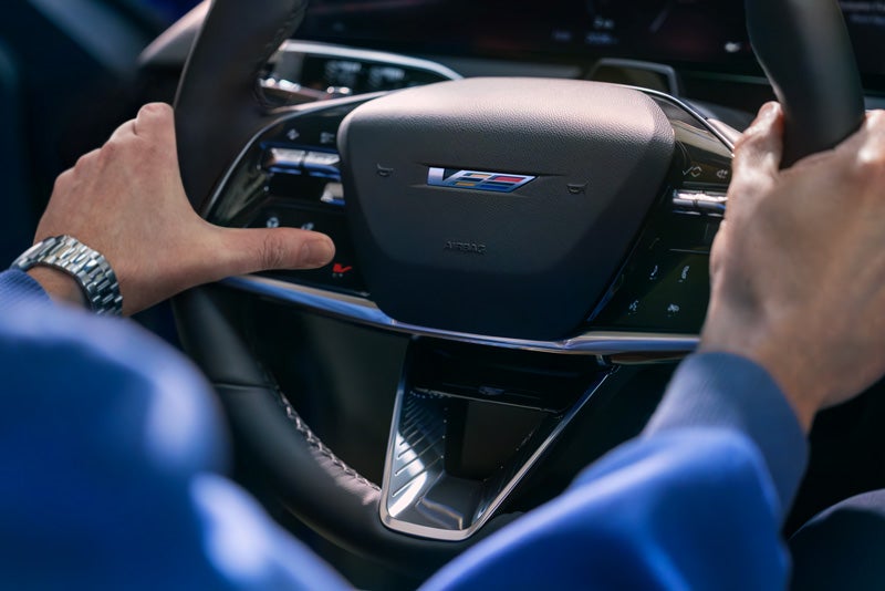 Close-up of a Man About to Press the V-Button on the 2026 OPTIQ-V Steering Wheel | Swickard Cadillac Anchorage in Anchorage AK